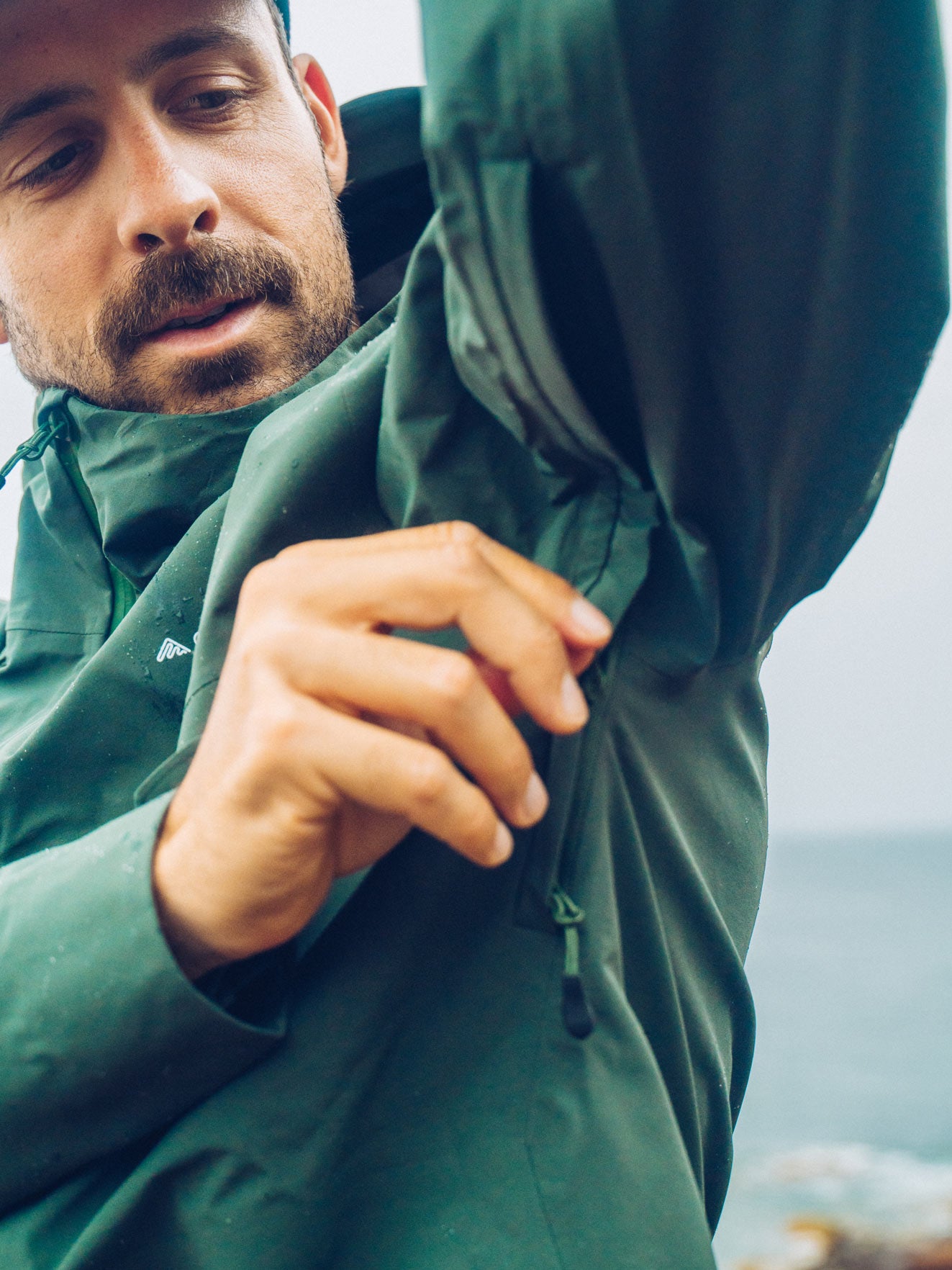Hiker raising his arm to show the articulated sleeve and underarm zip of a green Cortazu shell