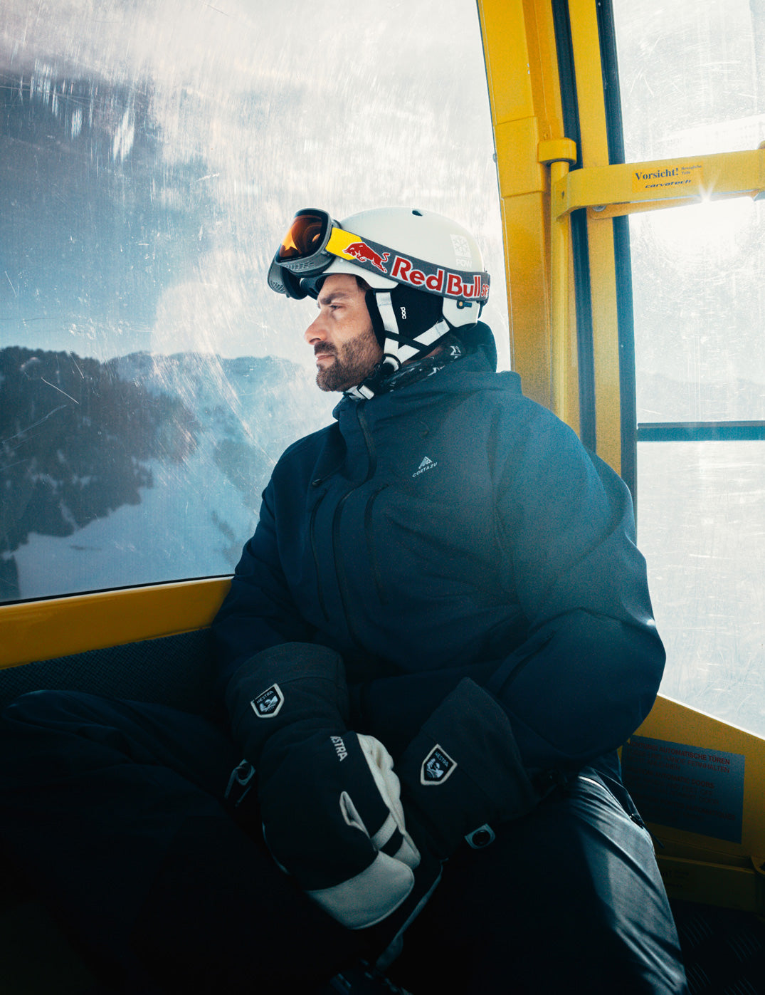 Person in ski gear sitting on a ski lift with snowy mountains in the background