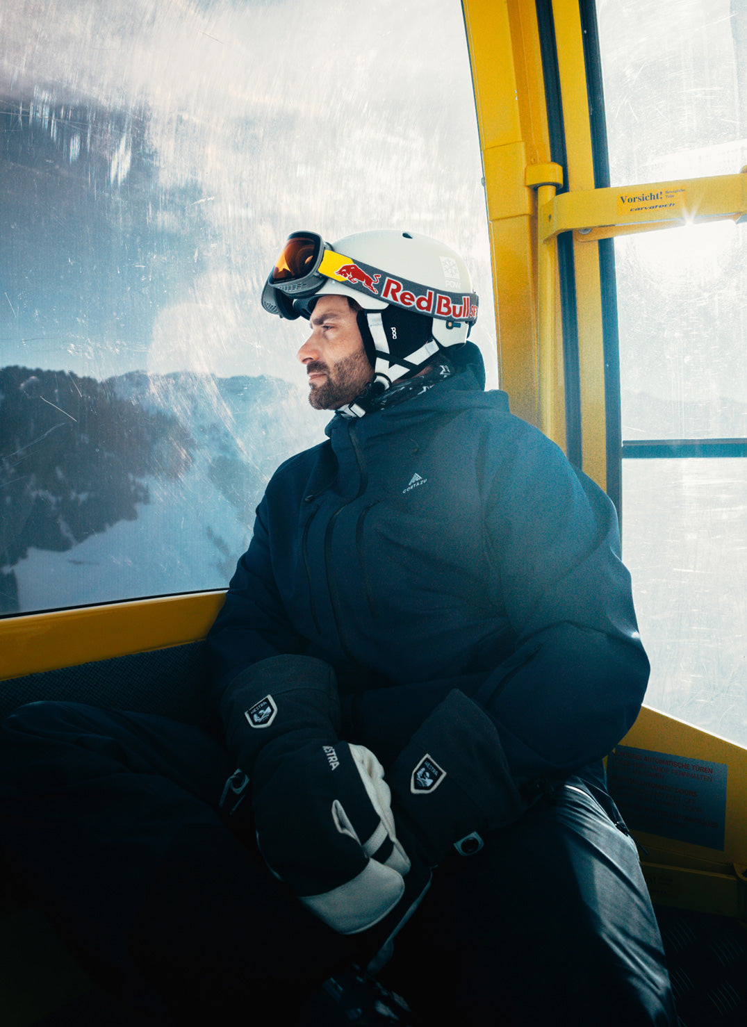 Person in ski gear sitting on a ski lift with snowy mountains in the background